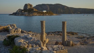 Two old columns in the foreground with a sunny island and blue water in the background, Agios