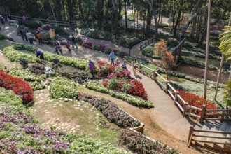 Tourists walking past colorful flowers and lush gardens while laborers maintain the grounds of the