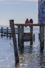 Man and woman sitting on a concrete platform at the base of the graffiti, covered Broadwater Beach
