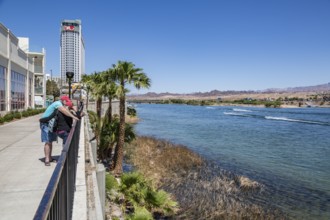 Couple looking at cell phone on sidewalk overlooking jet ski activity on the Colorado River in