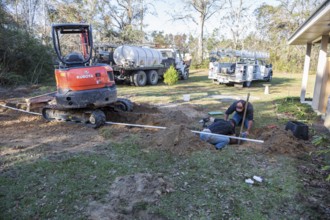 Workers installing pipe connecting new water well to house plumbing in rural area of Gulfport,