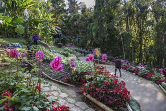 Tourists walking past colorful flowers and lush gardens while laborers maintain the grounds of the