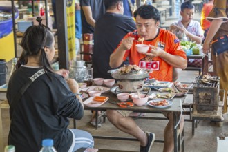 Thai couple cooking on a hot pot and eating at a buffet style outdoor restaurant in Chiang Rai