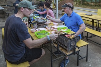 Male American missionaries cooking their food on a charcoal grill and hot pot at a buffet style