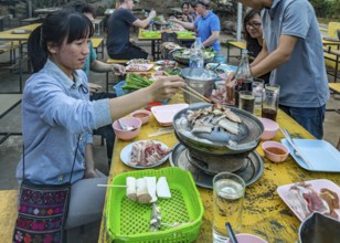 Thai woman cooking fish on a charcoal hot pot at a buffet style outdoor restaurant in Chiang Rai