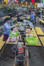 Thai man and woman cooking on a charcoal hot pot and grill at their table in a buffet style outdoor
