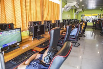 Thai men and boys watching online sports and playing video games online at an Internet gaming