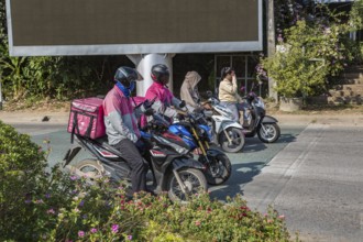 Food delivery drivers and other Thai motor scooter riders at a traffic light in Chiang Rai,