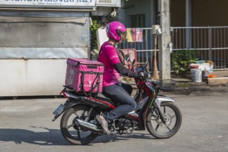 Food delivery drivers and other Thai motor scooter riders at a traffic light in Chiang Rai,