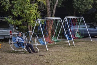 Thai man sitting alone on a childs playground swing in Chiang Rai, Thailand