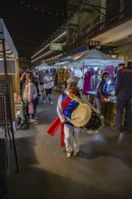 Cheery Thai woman beating a drum as she dances through the Night Market in downtown Chiang Rai,