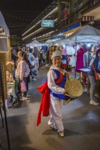 Smiling Thai woman beating a drum as she dances through the Night Market in downtown Chiang Rai,