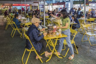 Thai mother and daughter preparing a meal in a hot pot at their table at the night market in