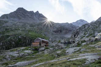 Mountain hut Elberfelderhütte in front of a rocky mountain landscape, sun star in the morning, in