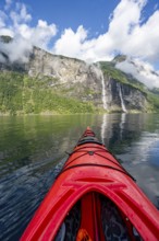 Kayak trip on the Geirangerfjord with waterfall The Seven Sisters, tip of a red kayak in the fjord,