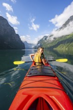 Kayak trip on the Geirangerfjord, young woman paddling in a red kayak, atmospheric fjord landscape,