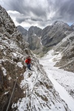 Mountaineer on a rope-secured path in a steep rocky mountain landscape with fresh snow in summer,