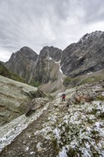 Mountaineer on hiking trail in steep rocky mountain landscape with fresh snow in summer, behind