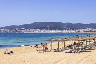 Sand beach by the blue mediterranean sea with sunbathing people at sun lounger and the palma city