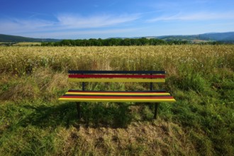 Bench in German colours with a wide view of a golden grain field and blue sky, summer, Germerode,