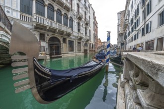 Traditional gondola moored in venice canal with turquoise water, near a bridge and old buildings,