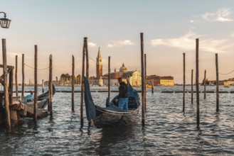Gondolier preparing his gondola in venice, italy, at sunset, with the church of san giorgio