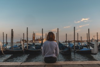 Young woman enjoying the sunset over the venetian lagoon with gondolas moored in the foreground and