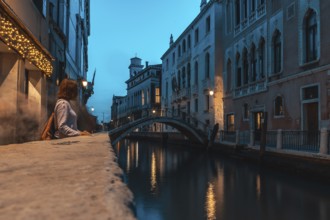 Young woman contemplating venice's canal at blue hour, with a small bridge and typical venetian