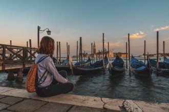 Young woman admiring gondolas and san giorgio maggiore church in venice, italy, during a beautiful