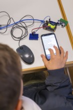 Child operating smartphone next to electronic devices on a table, Youth Research Centre Nagold,