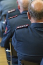 Men in uniforms sit lined up in a meeting room