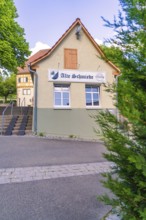 Small traditional building with sign, surrounded by trees and road, Deufringen, Aidlingen, Germany
