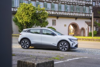 White car in front of a row of traditional half-timbered houses, surrounded by greenery in summer,