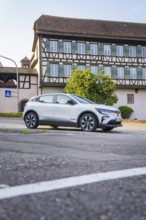 White car parked on an urban street in front of a large, traditional half-timbered house in summer,