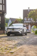 A white car on a cobbled street in a village with half-timbered houses and a summery atmosphere,