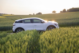 White electric car drives through a green field at sunset, Renault Megane, Deer E- Carsharing,