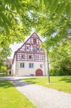 Half-timbered house with cobblestone path and surrounded by green trees under a clear sky, event