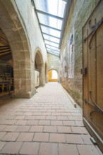 Corridor with medieval architecture, wooden chairs and wooden door, flooded with sunlight, event