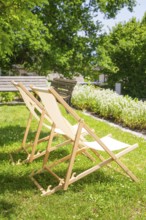 Two wooden deckchairs on a green lawn in the sunny summer garden under trees, event and wedding
