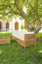 Wooden sofa under a tree in the garden with cushions, located in a shady forecourt, event and