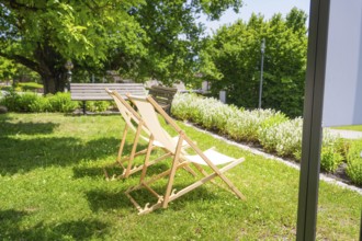 Two wooden deckchairs in the summer garden on a green lawn next to trees in the shade, event and