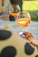 Person holding glass with orange coloured drink at a garden party in summer atmosphere, event and