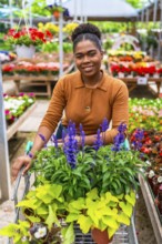 Happy young woman pushing a shopping cart, selecting vibrant flowers and plants while enjoying her