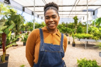 Portrait of a young african american woman smiling while working in a greenhouse, surrounded by