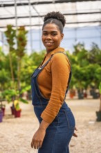 Confident young black woman tending to vibrant plants and flowers in a greenhouse, nurturing growth