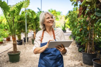 Smiling gardener working in a greenhouse, using a digital tablet while surrounded by vibrant plants