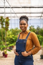 Confident agricultural worker smiling while holding her dungarees, surrounded by vibrant plants