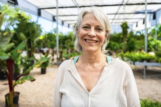 Portrait of a cheerful mature woman working joyfully in a greenhouse, surrounded by vibrant, lush