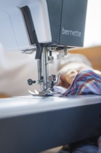 Close-up of the needle of a sewing machine sewing a chequered fabric in a well-lit room