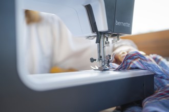 Details of the sewing process with needle and fabric in a well-lit environment, focus on the